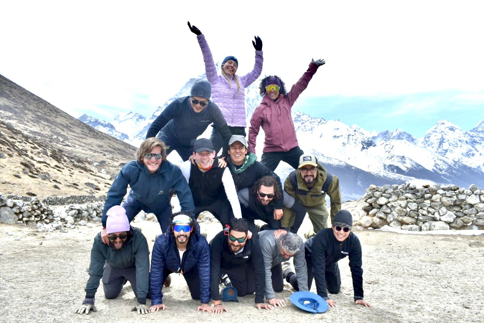 Viajeros formando una pirámide frente a montañas nevadas
