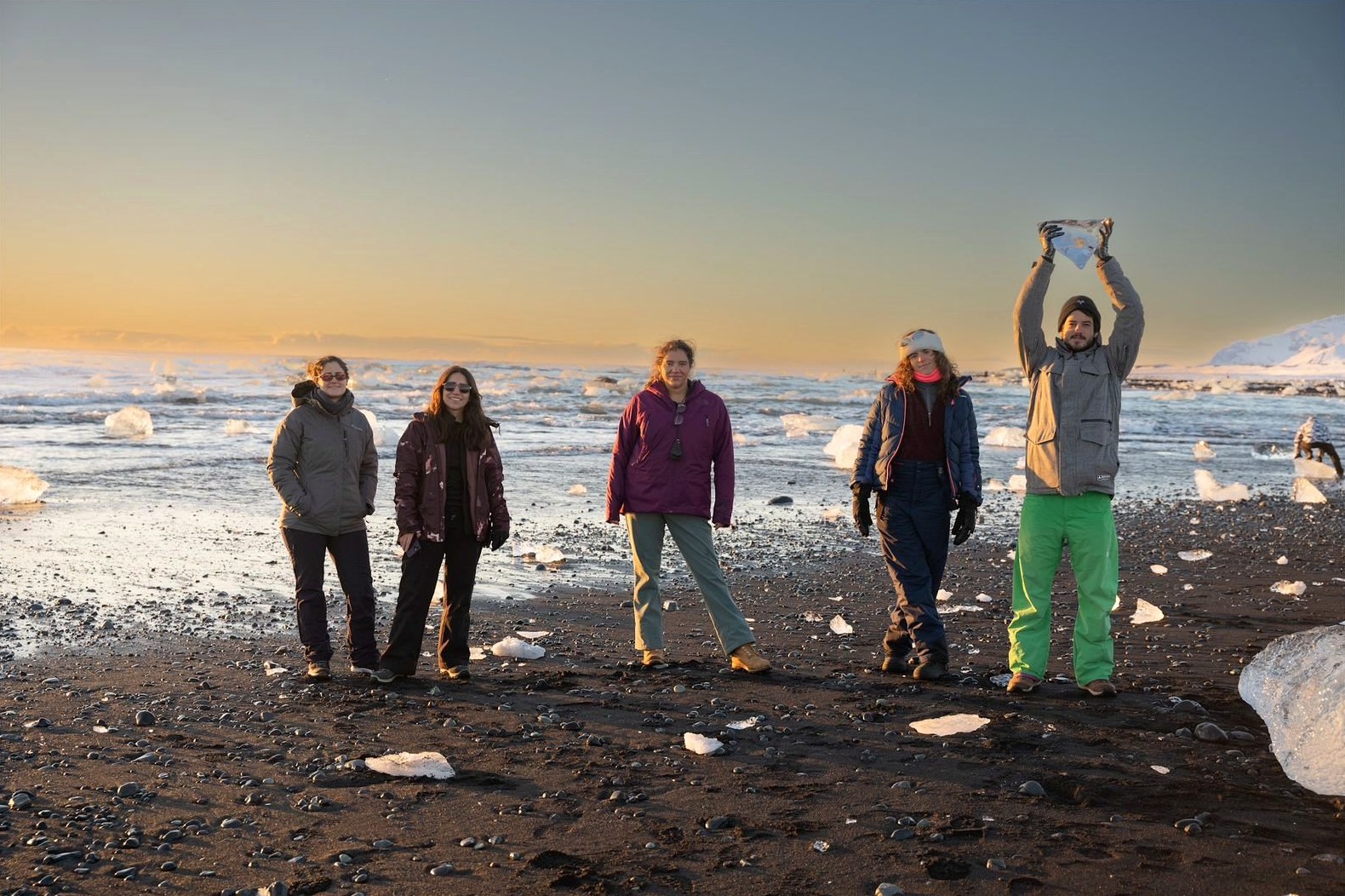 Grupo de viajeros en una playa de arena oscura al atardecer